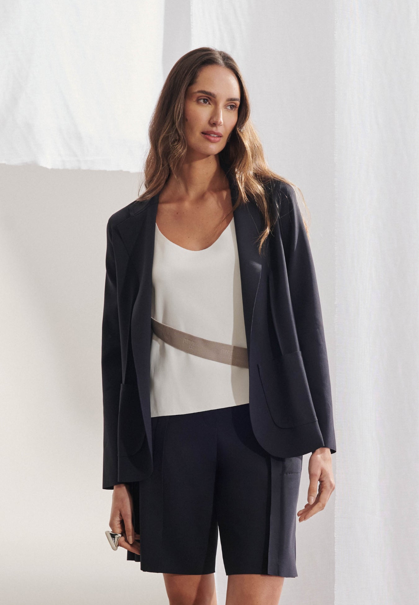 Blazer feminino de alfaiataria em malha tech com frente aberta sem botões. Gola com lapela entalhada clássica, pences verticais que moldam o corpo, manga longa com ombro estruturado e bolsos frontais chapados. Vista frontal.