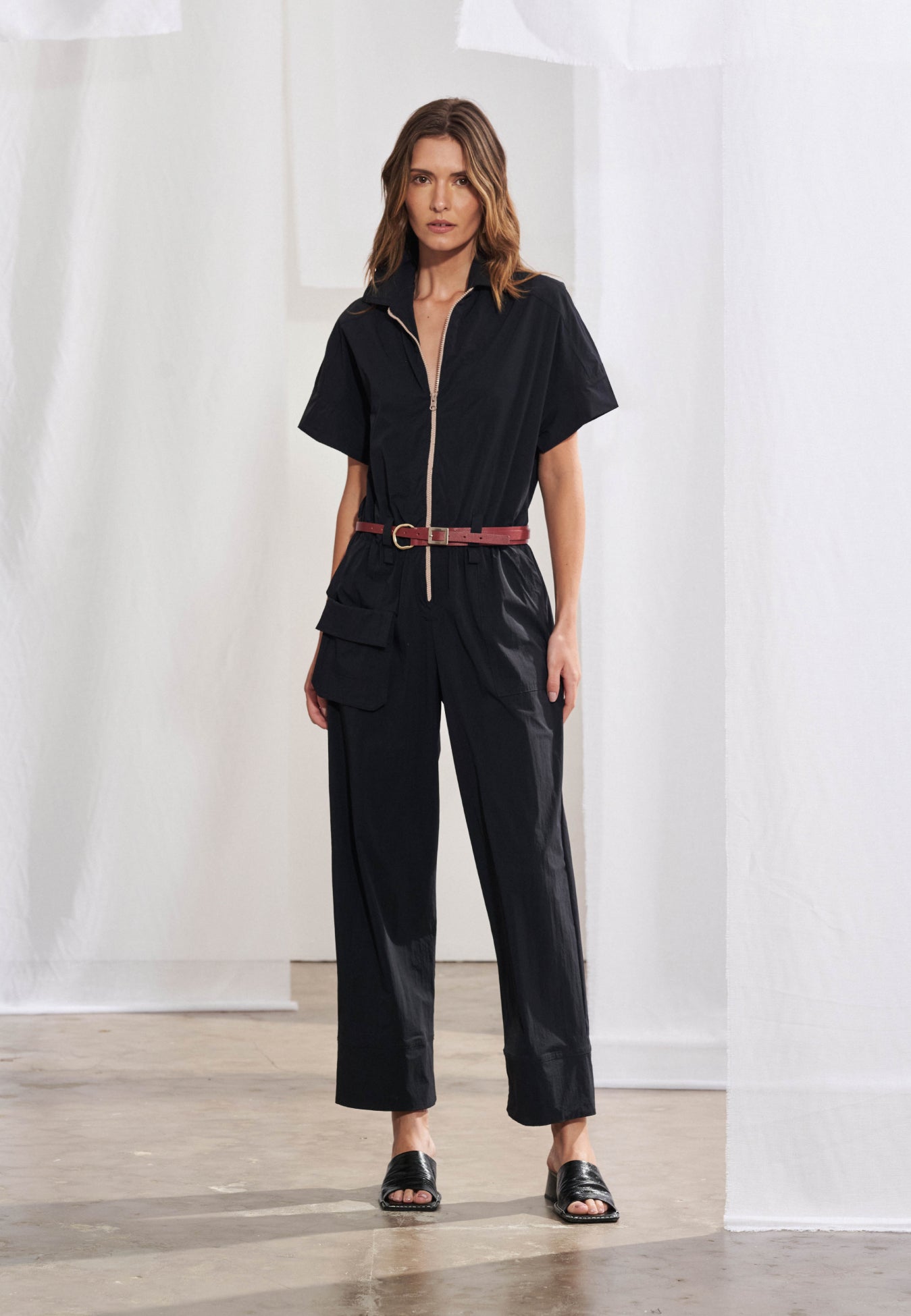 Macacão longo utilitário feminino em malha air. Gola colarinho esporte, fechamento frontal por zíper, bolsos frontais embutidos, bolso cargo com lapela retangular na lateral e cós com elástico embutido e passantes. Vista frontal e lateral.