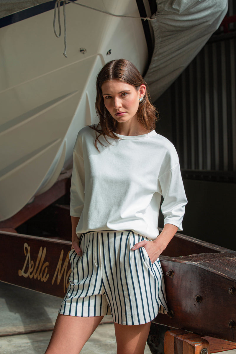 Modelo usando uma blusa branca de mangas longas e short com listras verticais azul marinho.